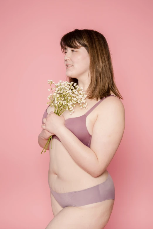 a woman in a bikini holding a bouquet of flowers, by Arabella Rankin, unsplash, mauve background, posing together in bra, on display, overweight