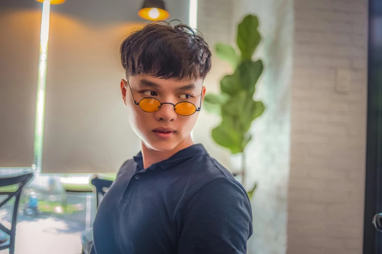 a young man wearing glasses standing in front of a window, inspired by Dai Jin, pexels contest winner, yellow hue, in style of lam manh, avatar image, 1 9 year old