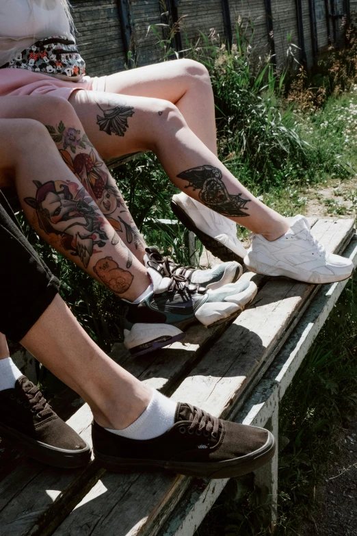 a group of people sitting on top of a wooden bench, a tattoo, inspired by Elsa Bleda, trending on pexels, running shoes, lo fi, couple, fully tattooed body