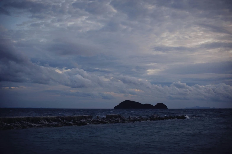 an island in the middle of the ocean under a cloudy sky, a picture, unsplash, romanticism, late evening, yoshifumi ushima, grey, brown