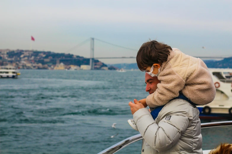 a man holding a child on the back of a boat, pexels contest winner, city bay bridge aqueduct, holiday season, genzoman, with a long