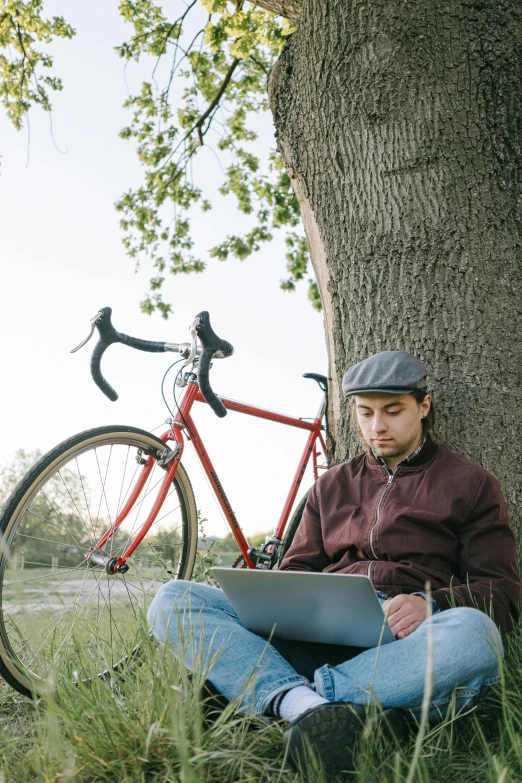 a man sitting under a tree using a laptop, a portrait, by Carey Morris, pexels contest winner, bicycles, no cropping, vintage inspired, charts