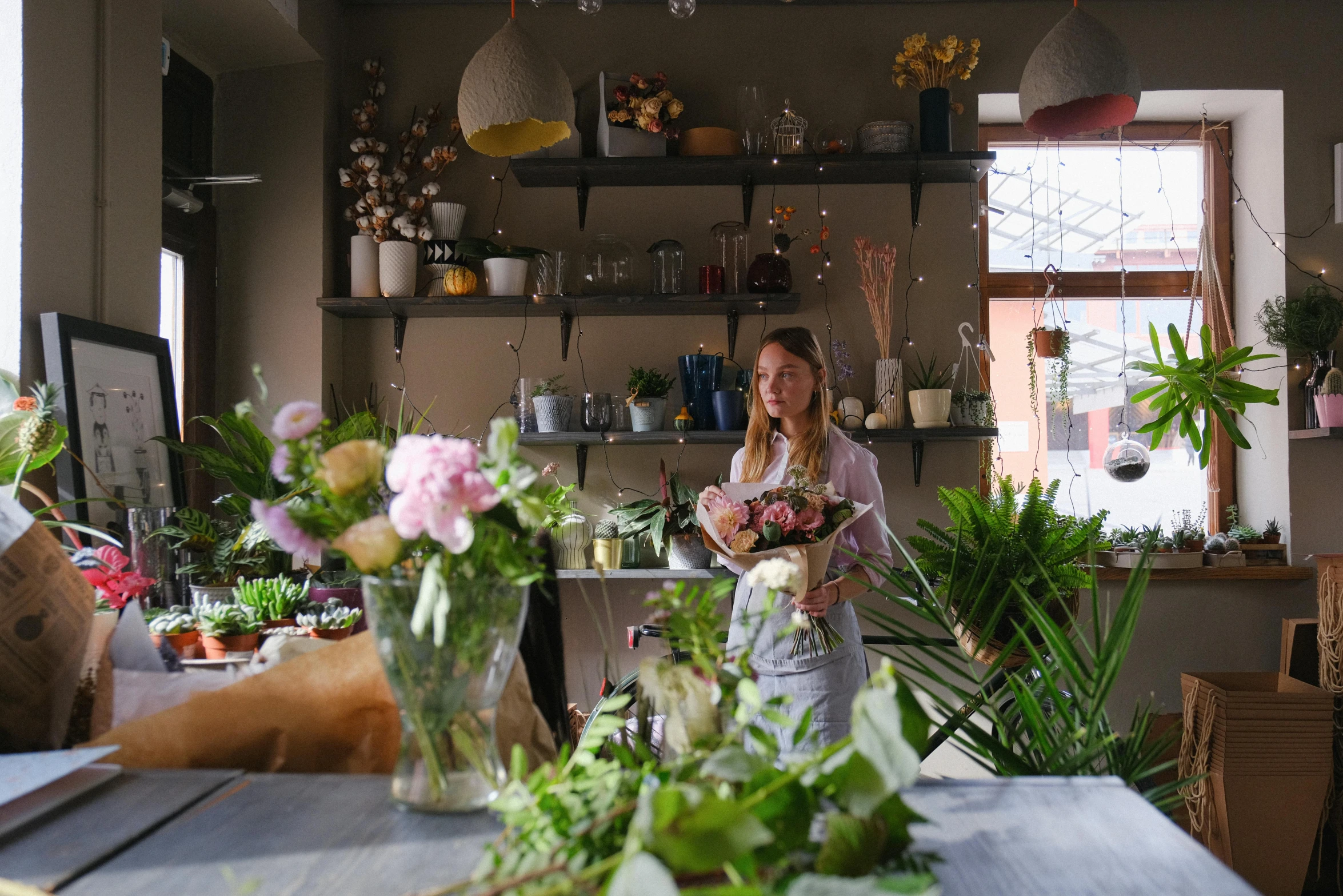 a woman standing in front of a table filled with flowers, quirky shops, flowers and stems, professionally done, good light