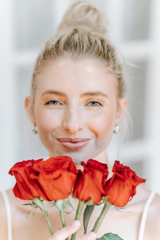 a woman holding a bunch of red roses in front of her face, trending on unsplash, blonde hair and blue eyes, pointé pose;pursed lips, smiling young woman, wedding