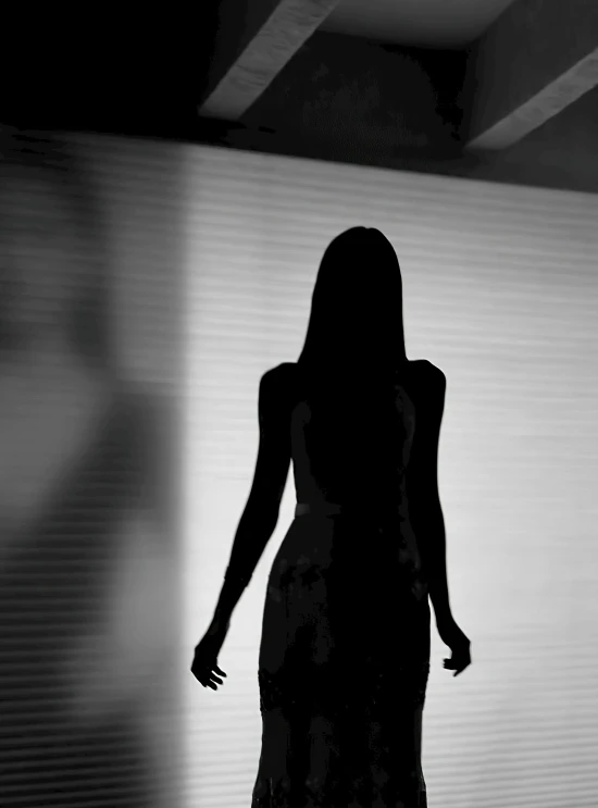 a black and white photo of a woman in a dress, inspired by Vanessa Beecroft, tumblr, eerie person silhouette, light dark long hair. apathetic, girl at a fashion show in hell, there is a glow coming from her