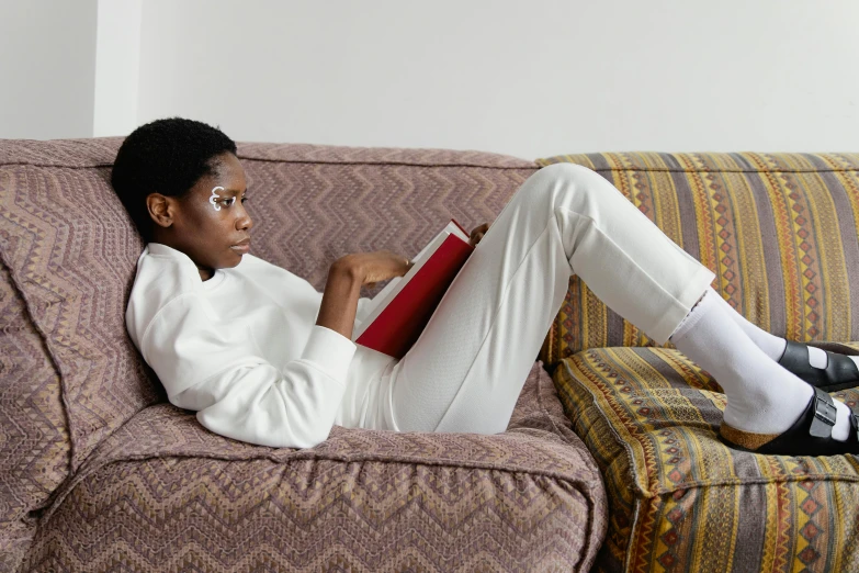 a woman sitting on a couch reading a book, inspired by Sarah Lucas, afrofuturism, wearing white suit, non binary model, in white turtleneck shirt, wearing a track suit