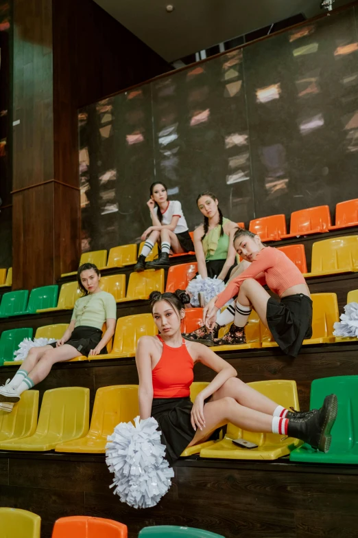 a group of people sitting on top of a bleachers, an album cover, by Julia Pishtar, colorful uniforms, bella poarch, indoor picture, nanquan