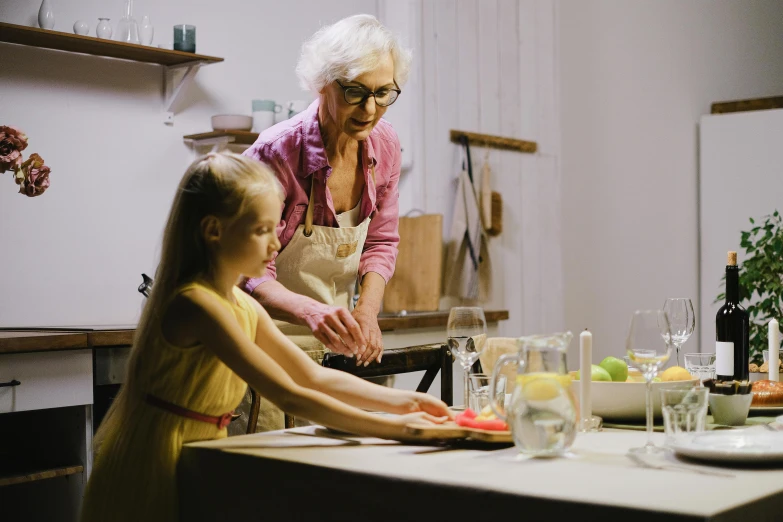 a woman standing next to a little girl in a kitchen, inspired by Henry Ossawa Tanner, pexels contest winner, hand on table, clay animation, an elderly, plating