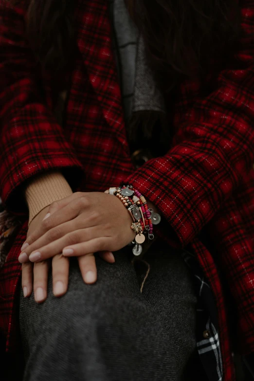 a close up of a person holding a cell phone, tartan garment, bracelets, sitting with wrists together, flannel