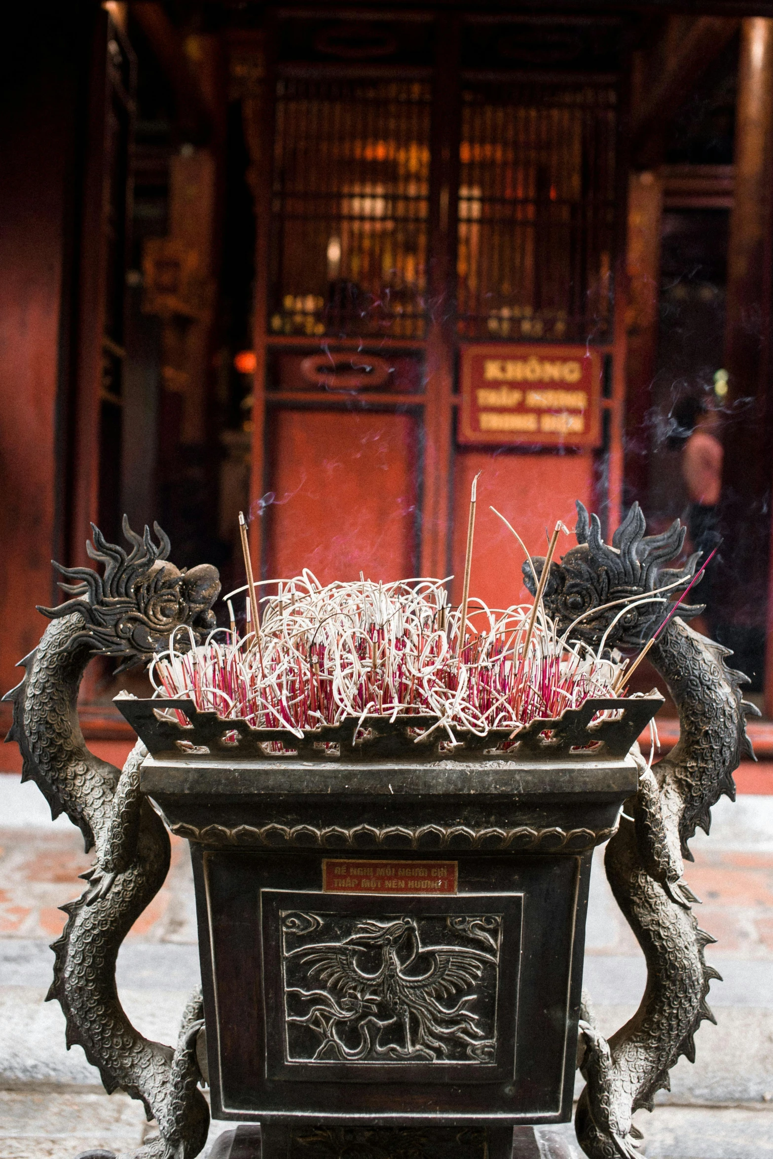 a metal dragon planter sitting in front of a building, incense smoke fills the air, vietnamese temple scene, ornate spikes, on a dark background