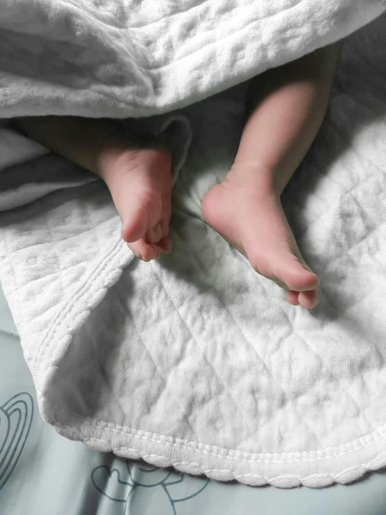 a baby laying on top of a bed covered in a blanket, by Helen Stevenson, happening, very close up foot shot, light grey mist, textured base ; product photos, currents