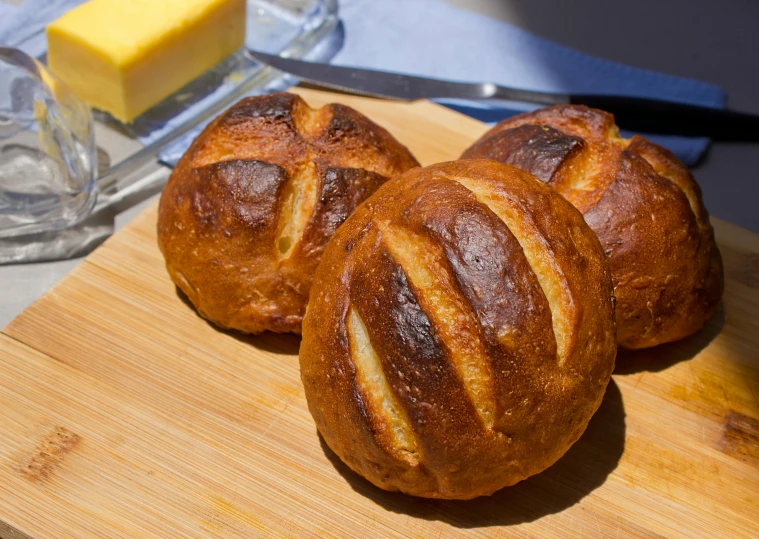 a bunch of bread sitting on top of a wooden cutting board, in the sun, profile image