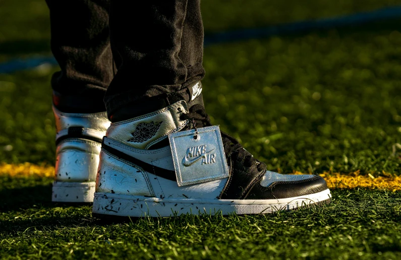 a close up of a person's shoes on a field, an album cover, by Joe Sorren, unsplash, realism, air jordan 1 high, black and silver, white gold skin, shot with sony alpha 1 camera