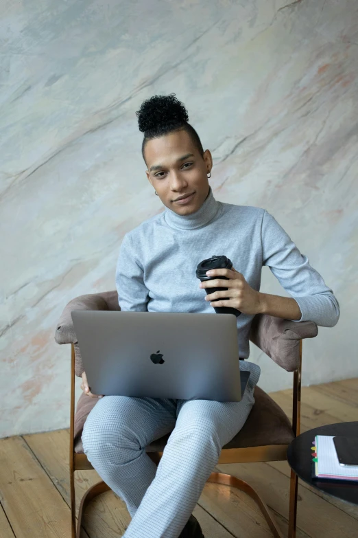 a man sitting in a chair with a laptop and a cup of coffee, a portrait, by Cosmo Alexander, trending on pexels, nonbinary model, hair styled in a bun, mixed race, beautiful androgynous prince