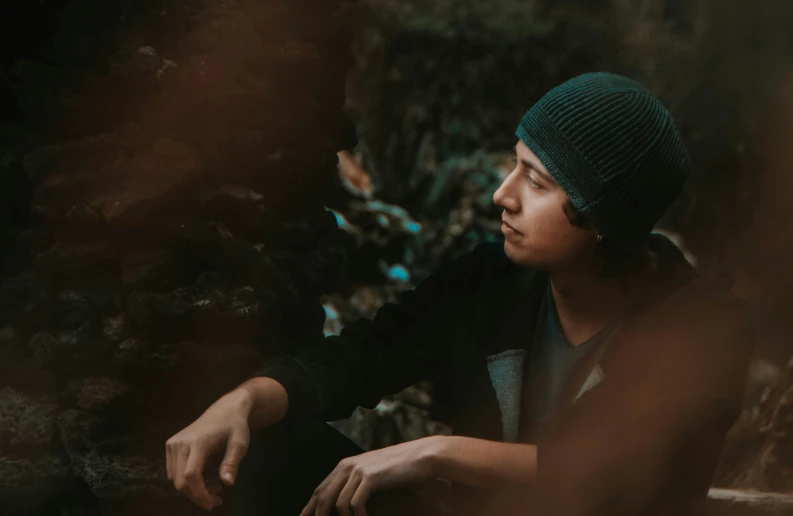 a man sitting on a rock in the woods, an album cover, inspired by Elsa Bleda, trending on pexels, realism, black beanie, detailed unblurred face, male teenager, thoughtful )