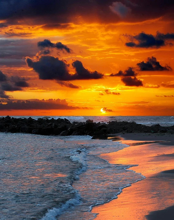 a person riding a surfboard on top of a sandy beach, it is sunset, on the ocean