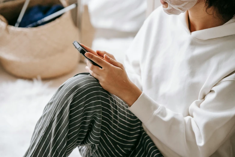 a woman sitting on a bed using a cell phone, trending on pexels, surgical gown and scrubs on, casual game, partially masked, wearing a white sweater