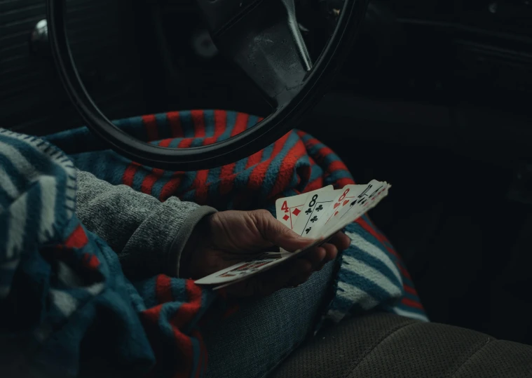 a person sitting in a car holding playing cards, by Elsa Bleda, pexels contest winner, hyperrealism, paul barson, cold, [ cinematic, childhood friend