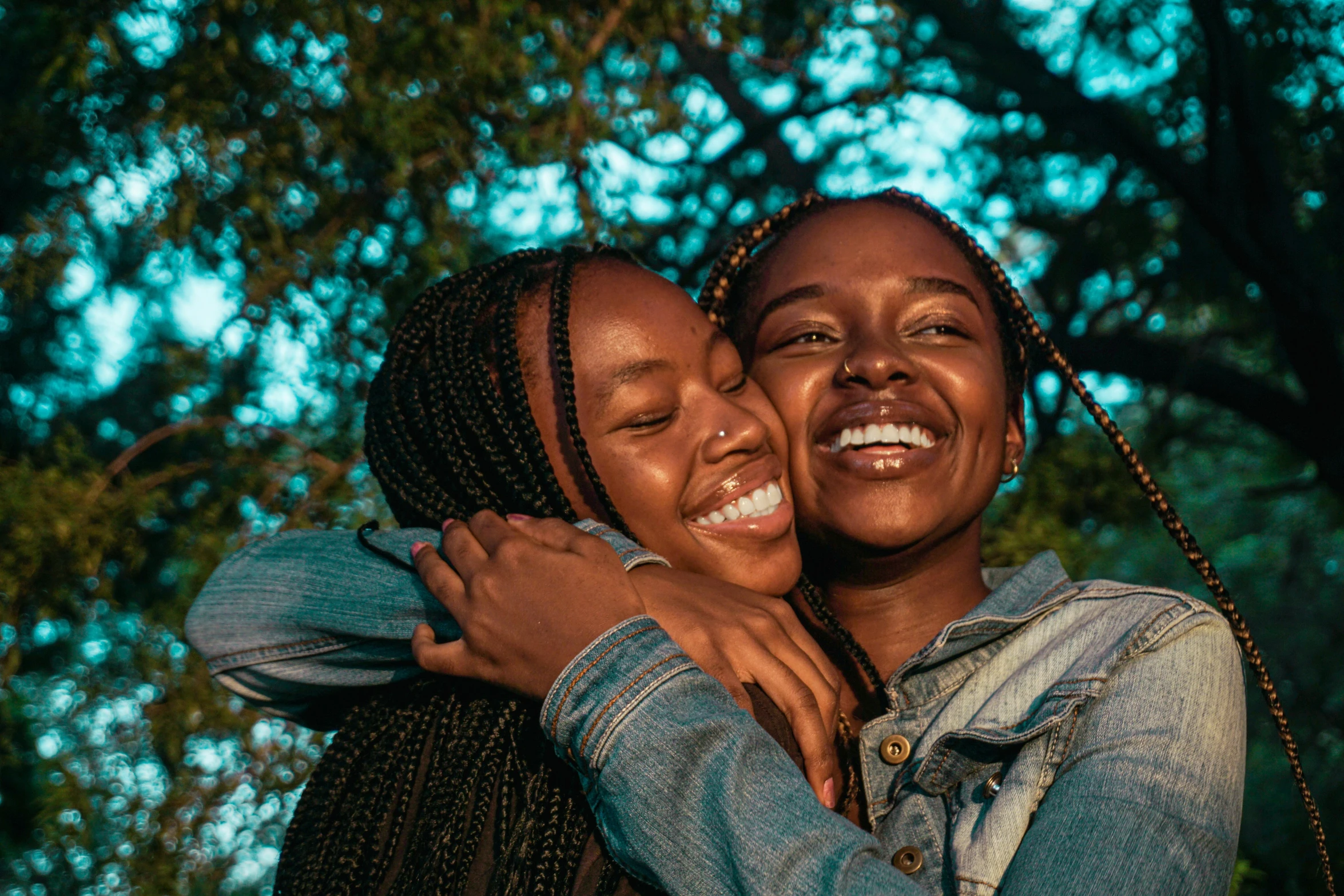 two women hugging each other in front of trees, by Matija Jama, pexels contest winner, black teenage girl, happy smiling, avatar image, brown skin