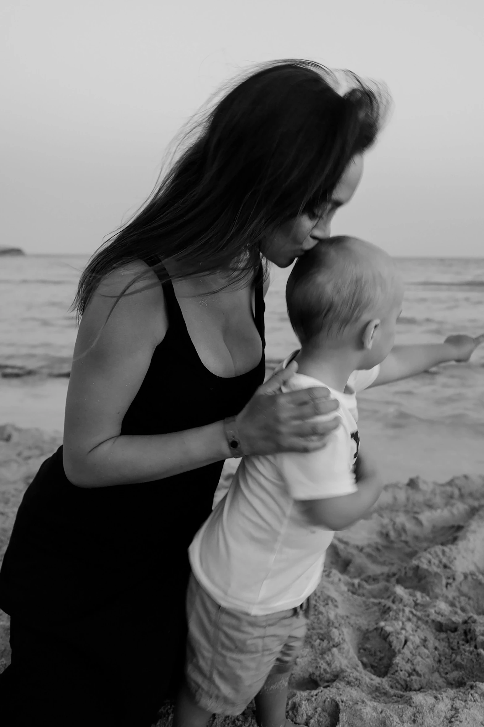 a woman holding a baby on the beach, a black and white photo, angelina jolie, artem chebokha, profile image, video