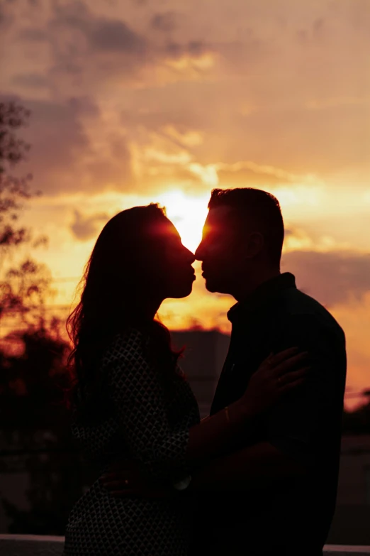 a couple standing next to each other in front of a sunset, pexels contest winner, romanticism, profile image, kissing, actual photo, photographs