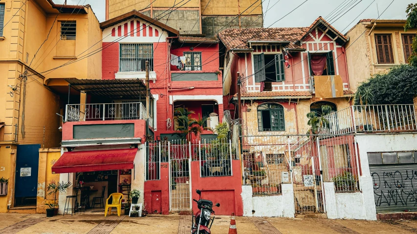 a motorcycle parked in front of a red building, inspired by Francis Souza, pexels contest winner, colombian jungle, houses on stilts, red white and gold color scheme, pink hues