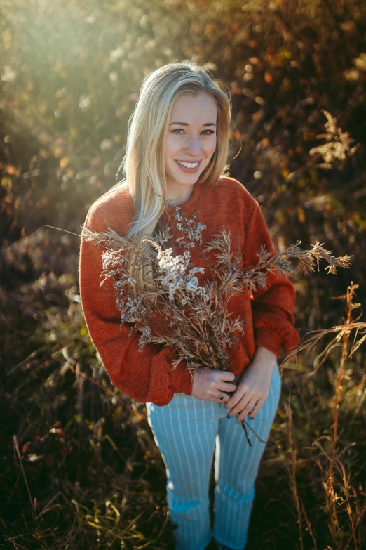 a woman standing in a field holding a bunch of flowers, a portrait, pexels contest winner, red sweater and gray pants, sydney sweeney, golden glow, instagram model