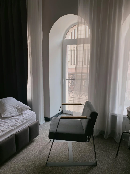 a bed sitting in a bedroom next to a window, a picture, sitting in a chair, in moscow centre, low quality photo, no text!