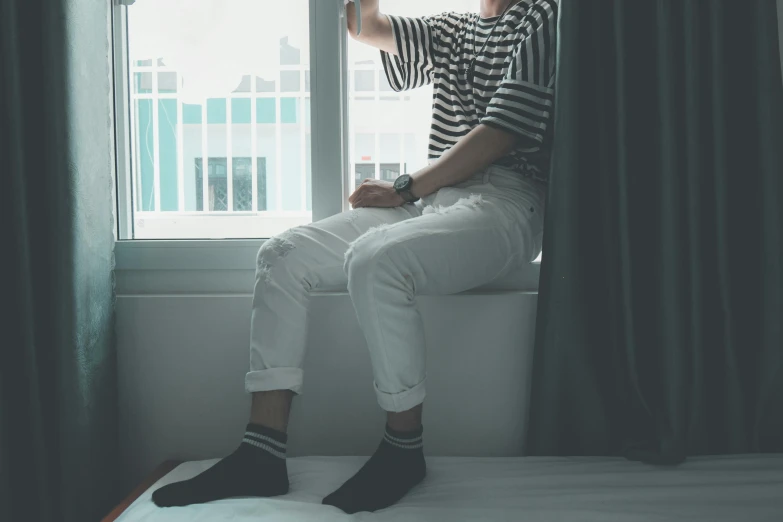 a man sitting on top of a bed next to a window, inspired by jeonseok lee, trending on pexels, white pants, striped socks, male teenager, outfit photo