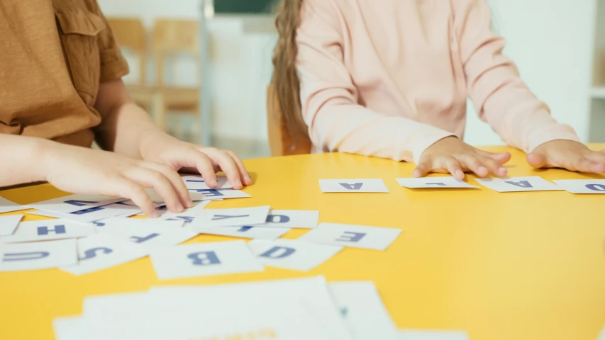 a group of children sitting at a table playing with letters, pexels contest winner, danube school, pair of keycards on table, lady using yellow dress, medium close up, 15081959 21121991 01012000 4k