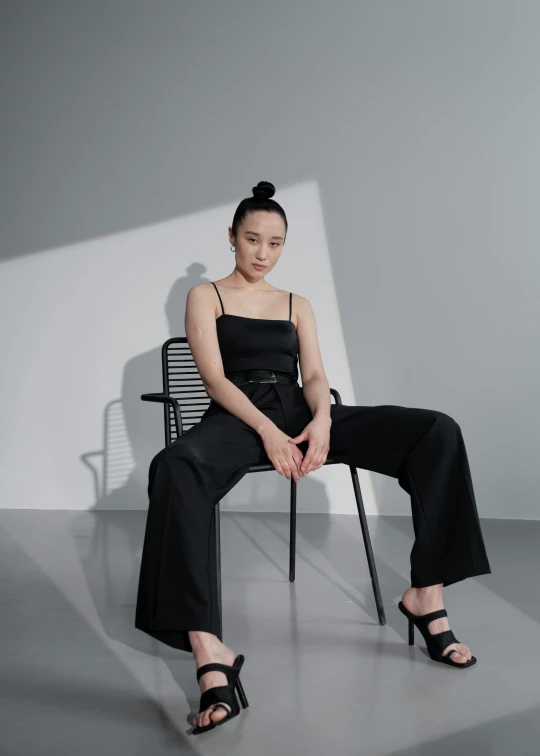 a woman sitting on a chair in a room, inspired by Wang Duo, wearing black camisole outfit, cinematic. by leng jun, curated collections, jumpsuit