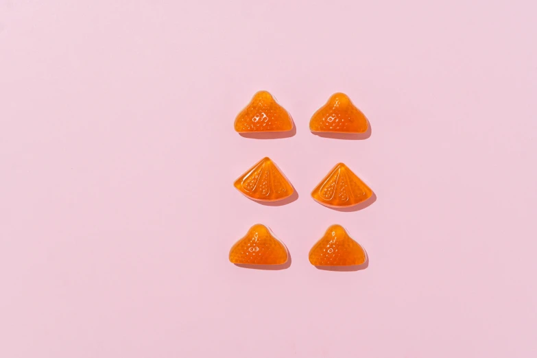 a group of orange candies sitting on top of a pink surface, a picture, by Nicolette Macnamara, shot with sony alpha, 6 pack, ffffound, arrow shaped