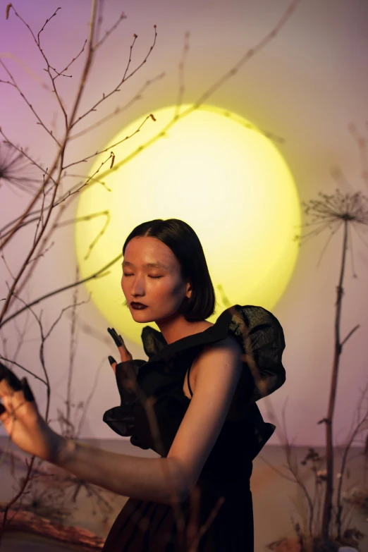 a woman in a black dress holding a cell phone, an album cover, inspired by Xie Sun, trending on pexels, surrealism, yellowish full moon, at a fashion shoot, profile pic, asian sun