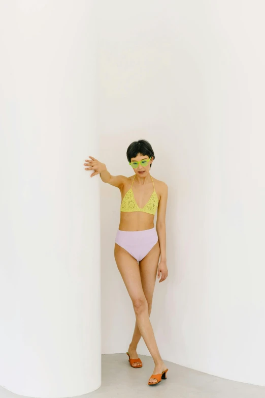 a woman in a bikini and sunglasses leaning against a wall, inspired by Ren Hang, trending on pexels, conceptual art, yellow purple green, standing in corner of room, bralette, jingna zhang