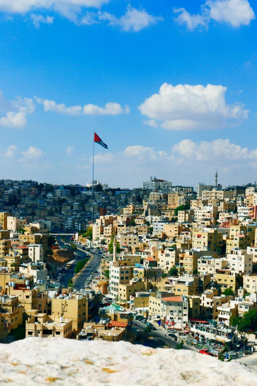 a view of a city from the top of a hill, an album cover, by Ibram Lassaw, trending on unsplash, hurufiyya, jordan, square, panoramic shot, red and black flags waving
