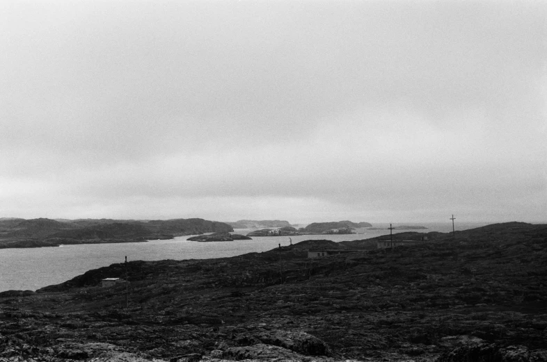 a black and white photo of a body of water, archipelago, eerie moorlands behind her, tri - x 4 0 0 tx, overcast!!!