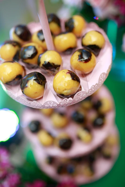 a tower of donuts sitting on top of a table, flying black marble balls, yellow and black trim, covered with pink marzipan, thumbnail