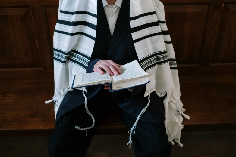 a man sitting on a bench reading a book, pexels, unilalianism, sukkot, wearing an ornate suit, white and black clothing, hebrew