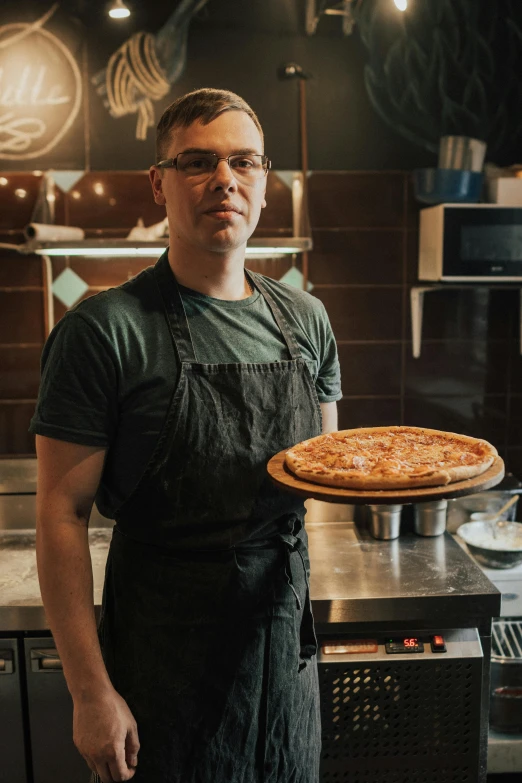 a man standing in a kitchen holding a pizza, daily specials, profile pic, lit from the side, handcrafted