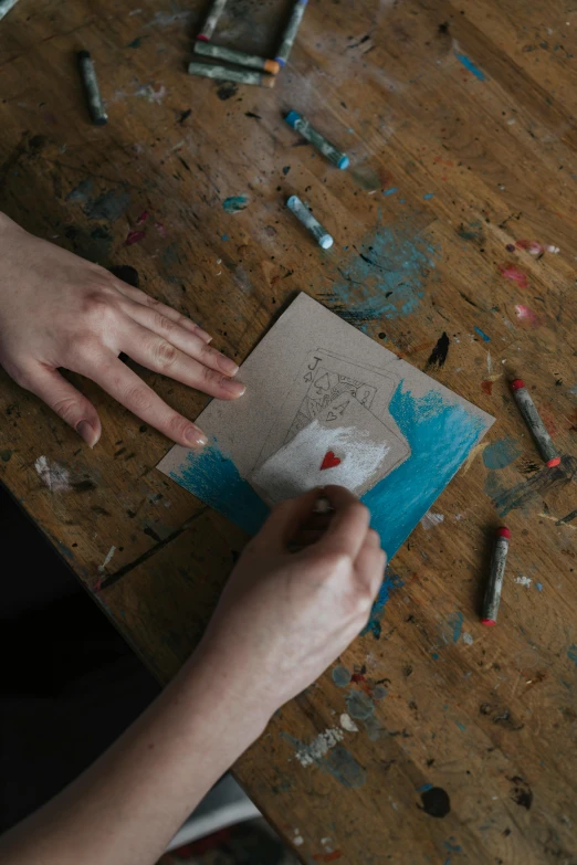 a person sitting at a table working on a piece of paper, inspired by Gerard David, pexels contest winner, arbeitsrat für kunst, blue paint on top, holding ace card, album cover, instagram picture