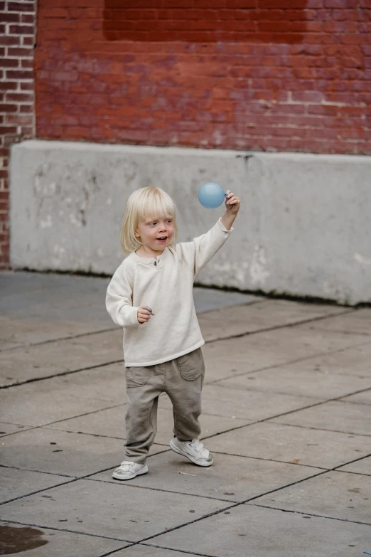 a little boy holding a blue ball in his hand, unsplash, happening, in a square, hammershøi, long sleeves, walkable