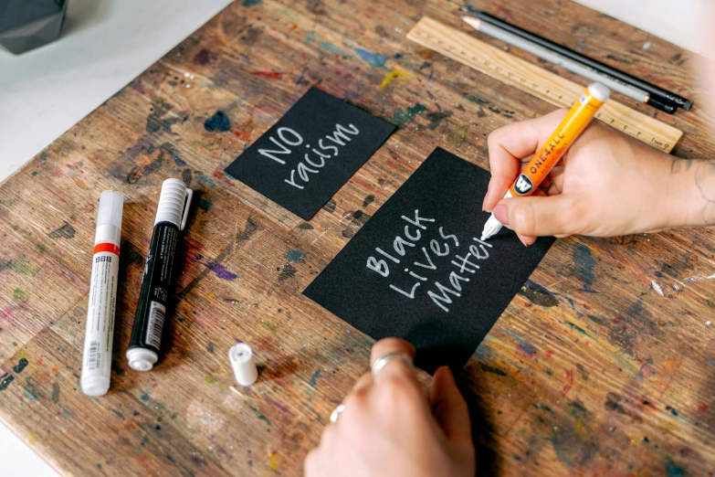 a person is writing on a piece of paper, by Matthias Stom, featured on unsplash, arbeitsrat für kunst, chalkboard, etsy stickers, white font on black canvas, placards