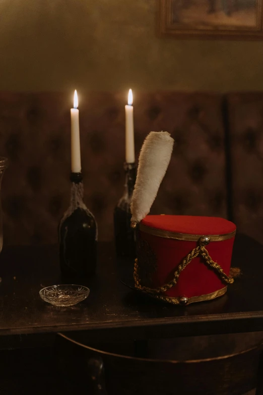 a red box sitting on top of a table next to a candle, by Elsa Bleda, renaissance, dressed in shako, inside a bar, napoleonic, dark lit candles