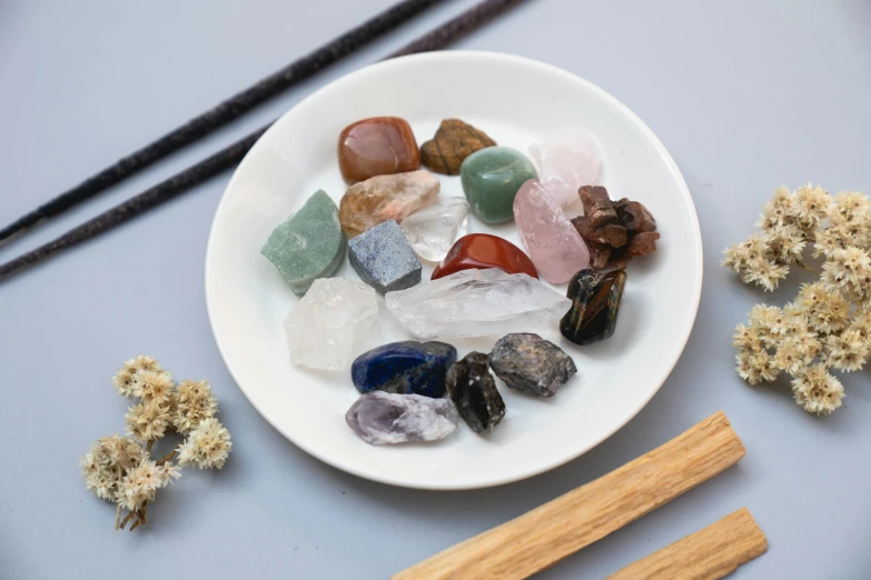 a white plate topped with lots of different types of stones, inspired by Asai Chū, unsplash, wooden magic wand, close up of single sugar crystal, small vials and pouches on belt, high quality product photo