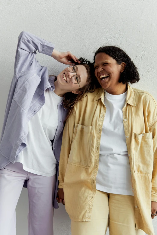 a couple of women standing next to each other, trending on unsplash, wearing a linen shirt, yellow purple, manically laughing, nonbinary model