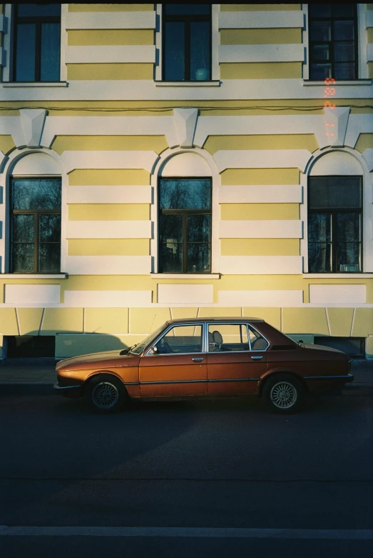 a red car parked in front of a yellow building, by Sergei Sviatchenko, 1990 photograph, golden sunlight, dirk dzimirsky, bmw