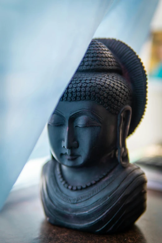 a buddha statue sitting on top of a wooden table, veiled face, wearing a black robe, hindu aesthetic, close up of face