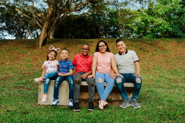 a group of people sitting on top of a wooden bench, a portrait, by Carla Wyzgala, pexels, puerto rico, of a family standing in a park, avatar image, sitting on green grass