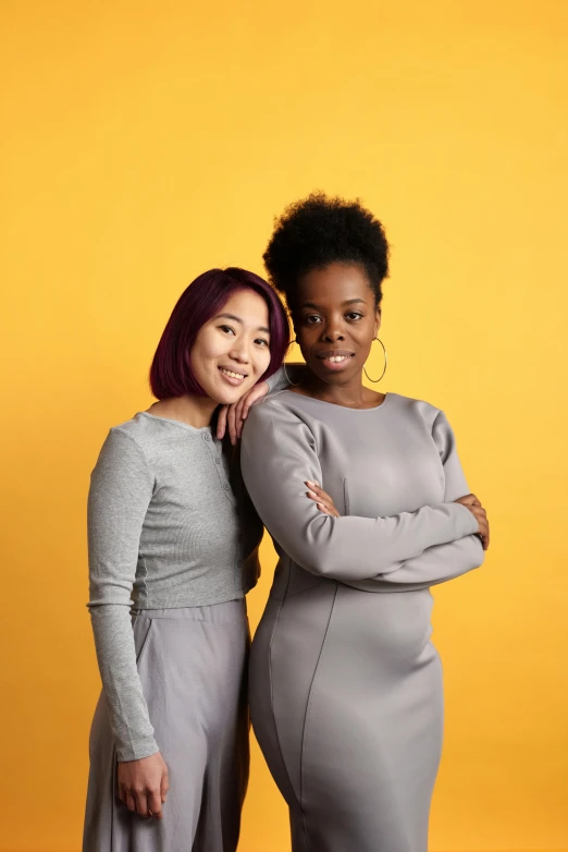 a couple of women standing next to each other, yellow backdrop, varying ethnicities, on a gray background, square