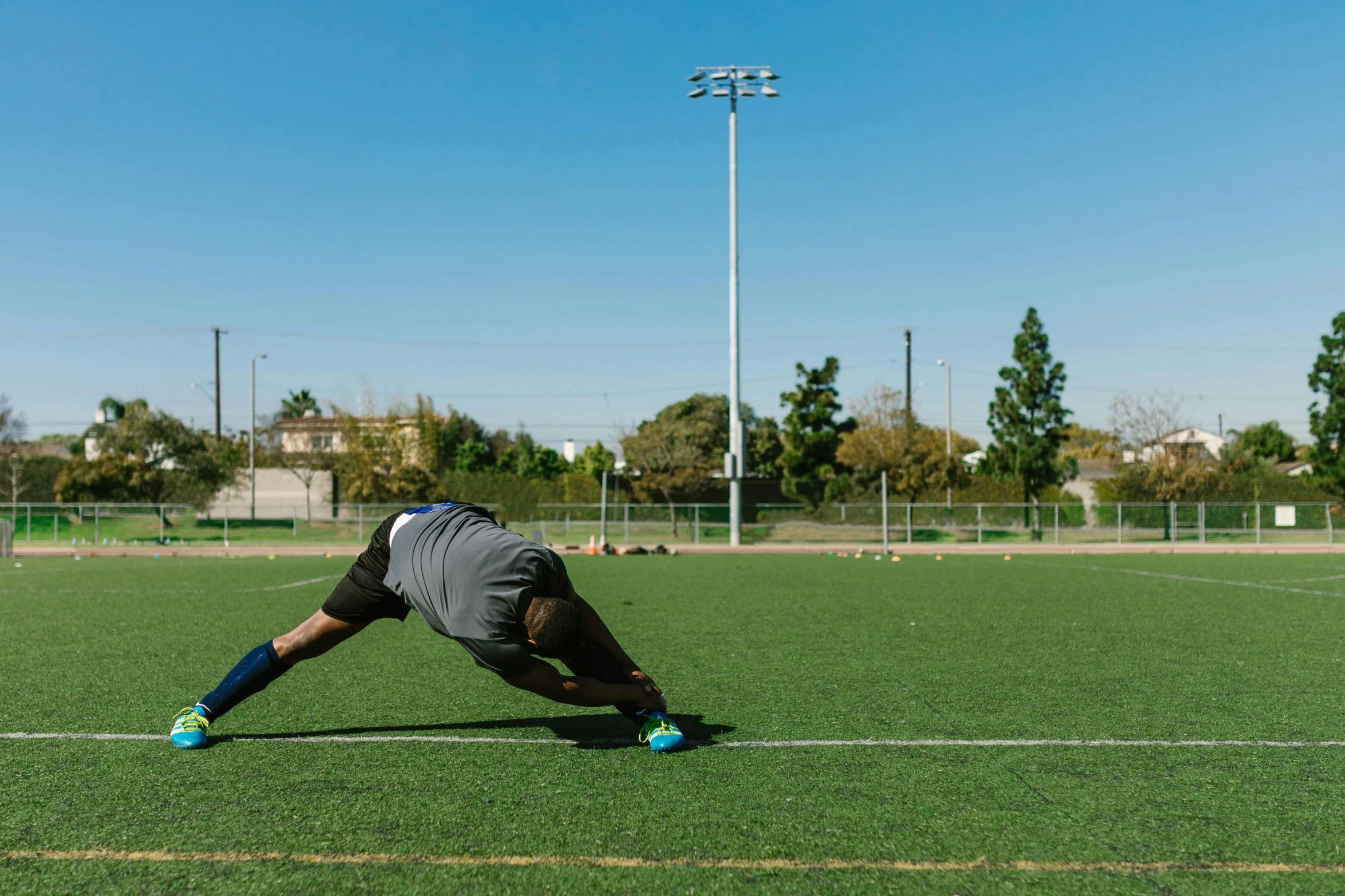 a man is stretching on a soccer field, by Ryan Pancoast, square, high resolution photo, cone, athletic crossfit build